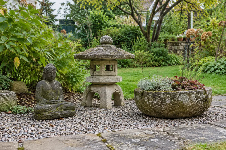 Buddha-Figur, japanische Steinlaterne und bepflanztes Steingefäß in einem Wohngarten